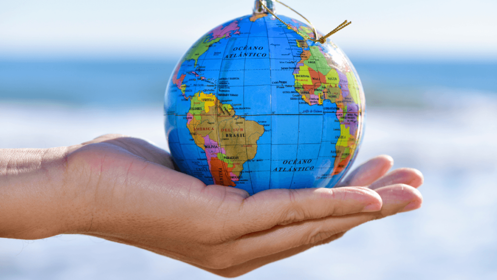 Mano sosteniendo un globo terráqueo frente al mar representando el concepto de qué es expat y el proceso migratorio